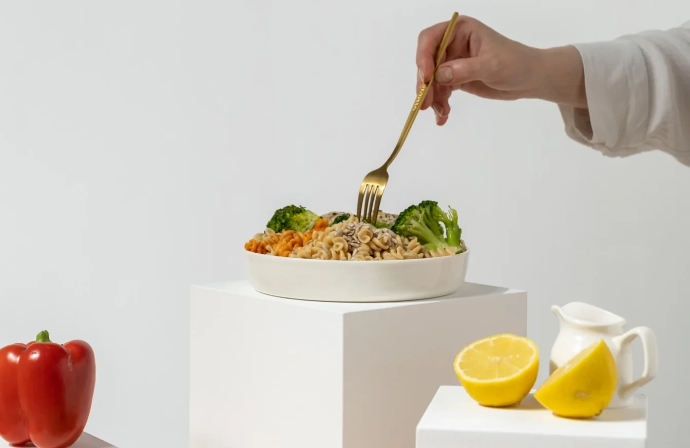 Primer plano de la mano de una mujer cogiendo un tenedor y un plato de pasta con verduras y semillas