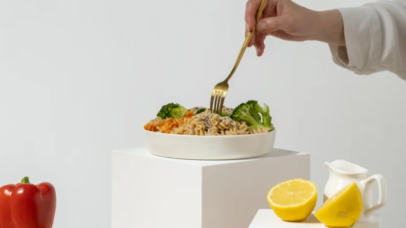 Primer plano de la mano de una mujer cogiendo un tenedor y un plato de pasta con verduras y semillas