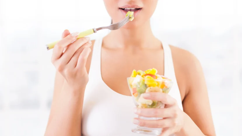 Imagen de una mujer con ropa deportiva mientras disfruta comiendo pequeños trozos de diferentes tipos de frutas